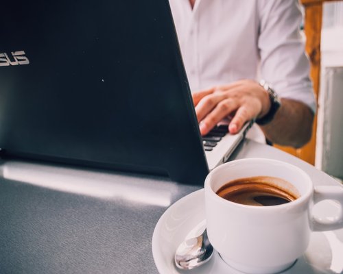 Persona trabajando frente a la computadora con un café
